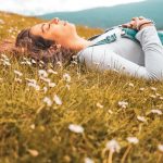 woman in blue long sleeve shirt lying on green grass field during daytime